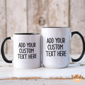 Two customizable white ceramic mugs with black handles and interiors, displayed side-by-side on a rustic white wooden surface with a weathered wood background. The mugs feature placeholder black text reading 'ADD YOUR CUSTOM TEXT HERE'.