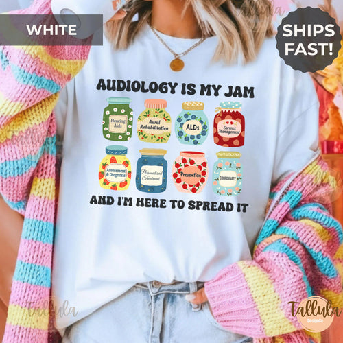 A T-shirt with a colorful jar-themed print and the text 'AUDIOLOGY IS MY JAM AND I'M HERE TO SPREAD IT'. Featuring cute jam jars design & descriptive words related to Audiology, hearing doctor.