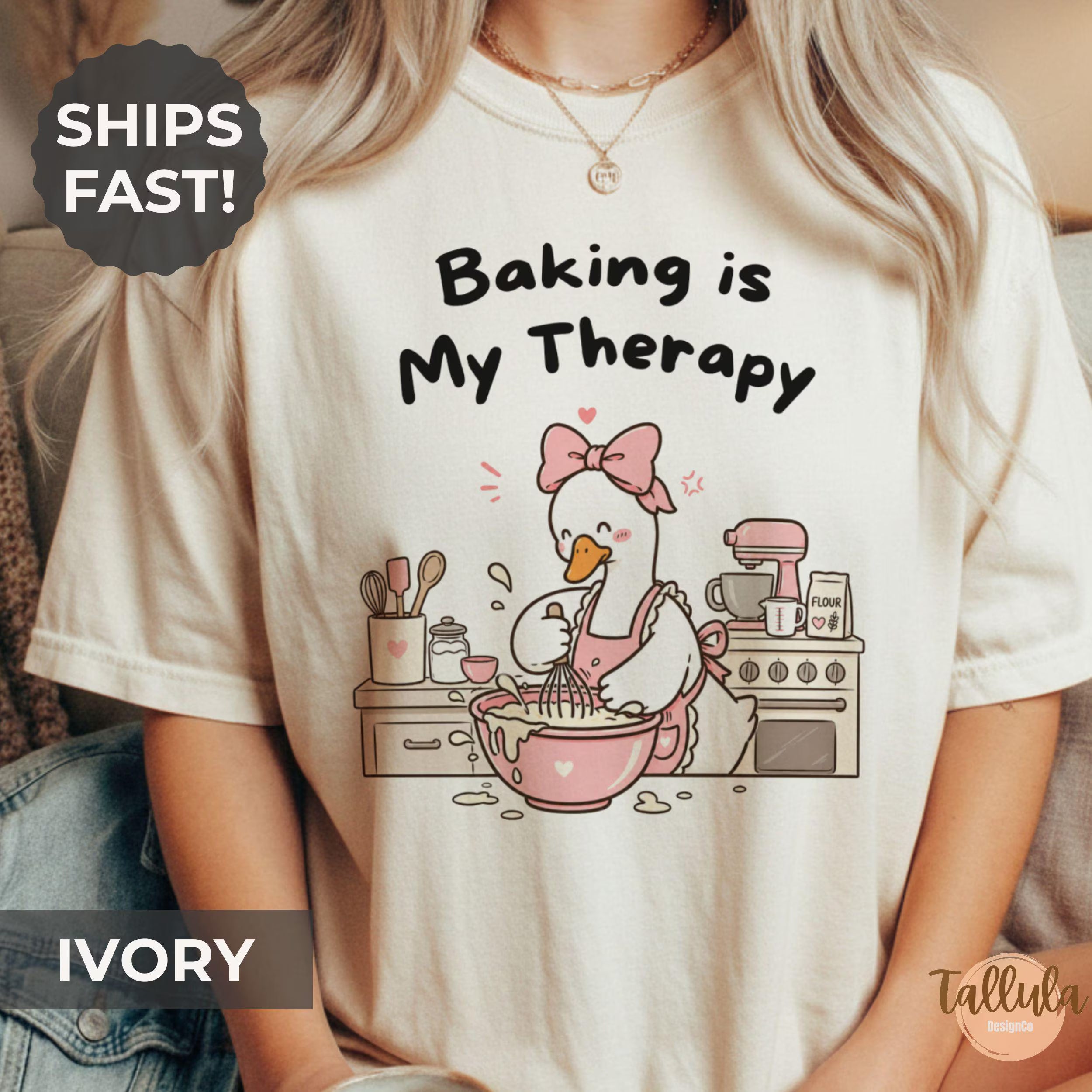 A graphic T-shirt with the text 'Baking is My Therapy' and a cartoon goose baking illustration with messy kitchen bench