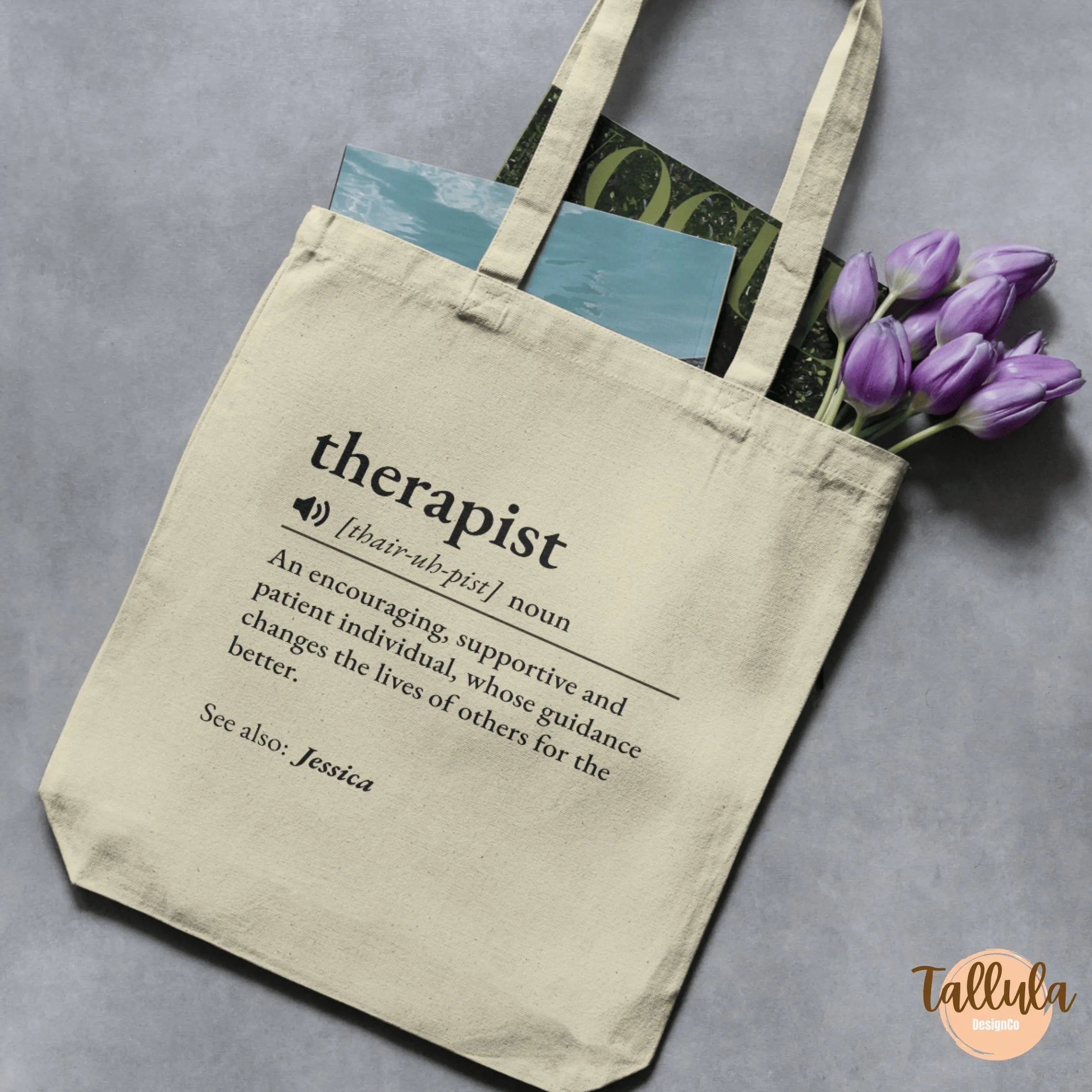 A cream canvas tote bag with printed black text defining the word 'therapist' in dictionary style with pronounce reading, personalized with name
