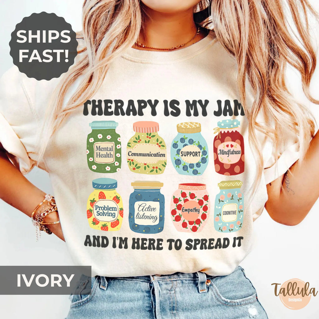  An ivory graphic t-shirt with a jam jars-themed graphic and the text 'THERAPY IS MY JAM AND I'M HERE TO SPREAD IT'. Featuring descriptive words for each jar, related to therapy, counseling, psychotherapy, mental health