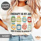  An ivory graphic t-shirt with a jam jars-themed graphic and the text 'THERAPY IS MY JAM AND I'M HERE TO SPREAD IT'. Featuring descriptive words for each jar, related to therapy, counseling, psychotherapy, mental health