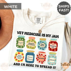 A white short-sleeve t-shirt with a colorful graphic of jars labeled with vet terms and the text 'VET MEDICINE IS MY JAM' and 'AND I'M HERE TO SPREAD IT'. The t-shirt featured the descriptive words related to vet doctor, veterinary technician assistant