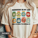 A comfort colors graphic t-shirt with the text 'MIDWIFERY IS MY JAM AND I'M HERE TO SPREAD IT' and eight colorful illustrated jam jars, featuring descriptive words on each jar related to midwife, doula, mother baby nurse, postpartum nurse, perinatal nurse